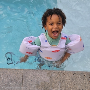 enfant joue dans l'eau avec sa veste de flottaison du design mini surfer, blanc avec des motifs de surfs colorés