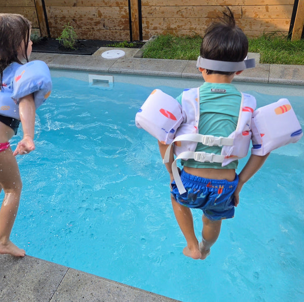 Enfants vue de dos sautent dans la piscine avec leurs flotteurs Sunnies